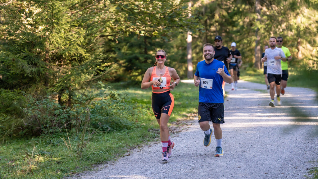 Eine Läuferin und ein Läufer sind auf der Eventstrecke des Achenseelaufs unterwegs. Sie befinden sich auf dem Bild umringt von Waldlandschaft.