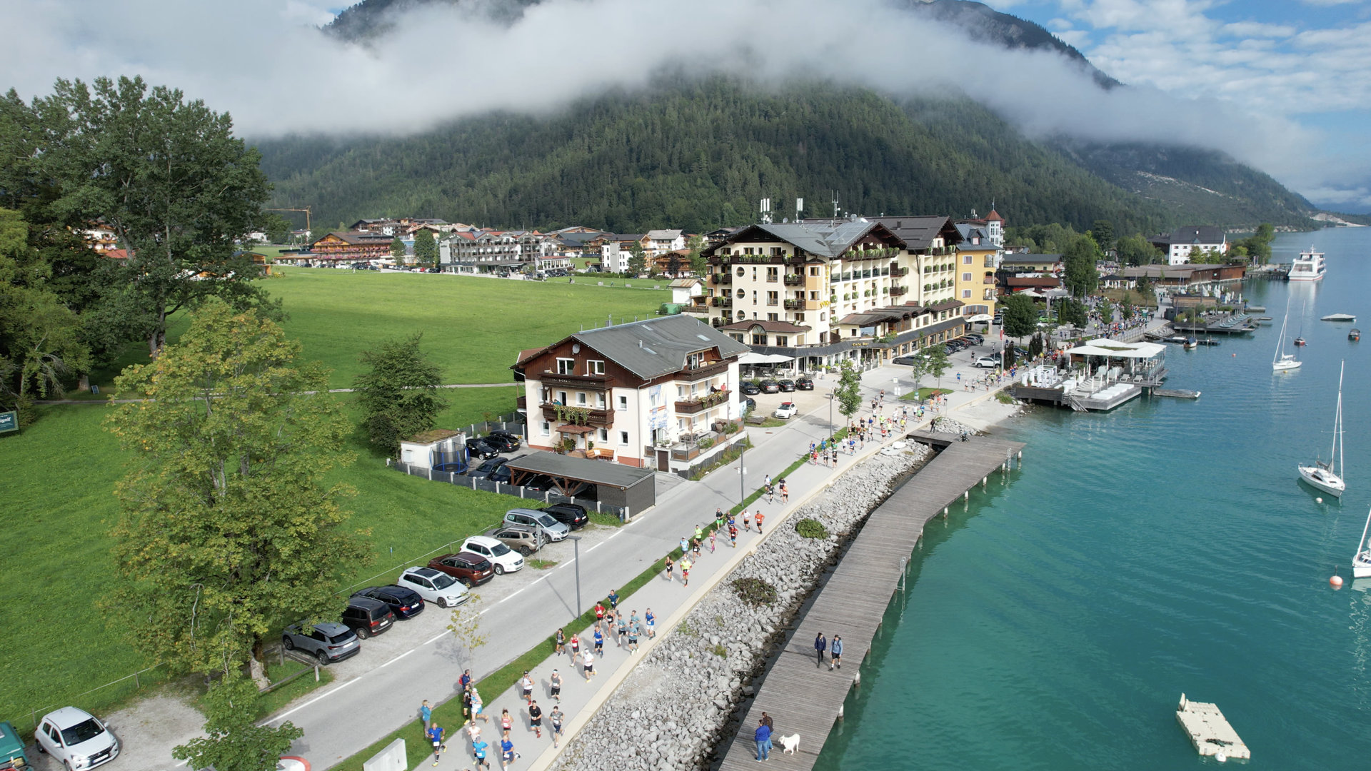 Teilnehmer des Achenseelaufs sind auf der Laufstrecke in Pertisau unterwegs. Links daneben sieht man die Parkmöglichkeiten.